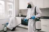 Pest control technician in a protective suit spraying along kitchen cabinets